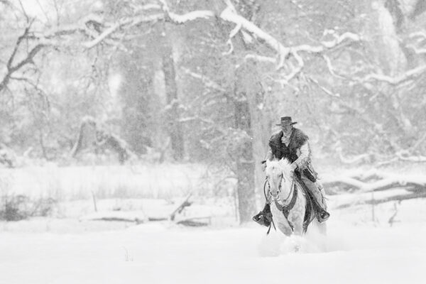cowboy riding horse in heavy snow storm black and white fine art photography